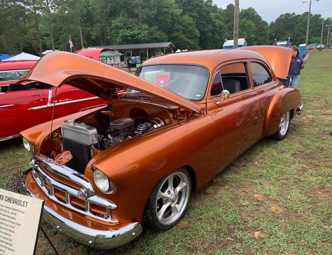 A bronze/brown vintage Chevrolet car with the hood open at a car show.