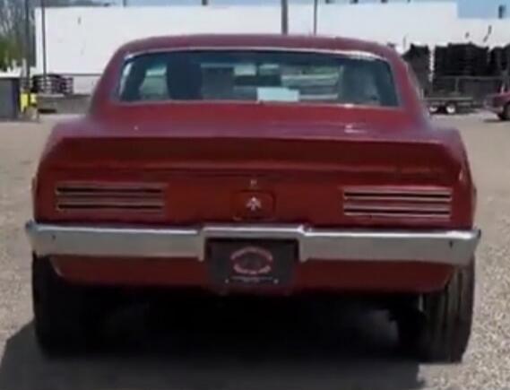 A red classic muscle car is shown from the rear, parked outdoors.