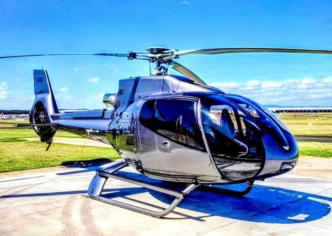 A modern grey helicopter is parked on an airfield under a clear blue sky.