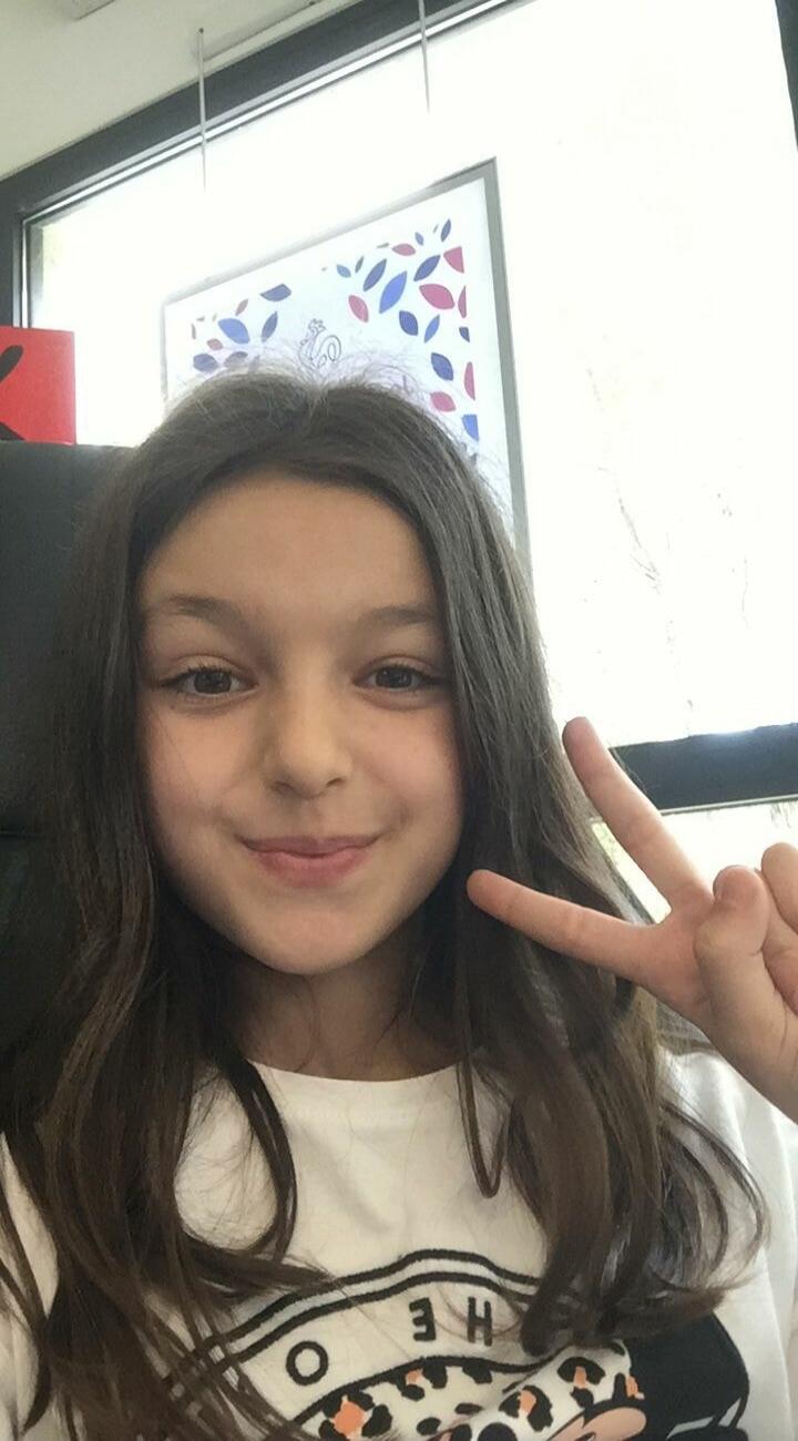 A young girl taking a selfie and making a peace sign.
