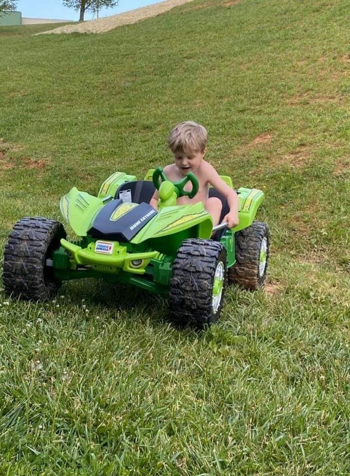 A young child driving a bright green ride-on toy car on a grassy hill.