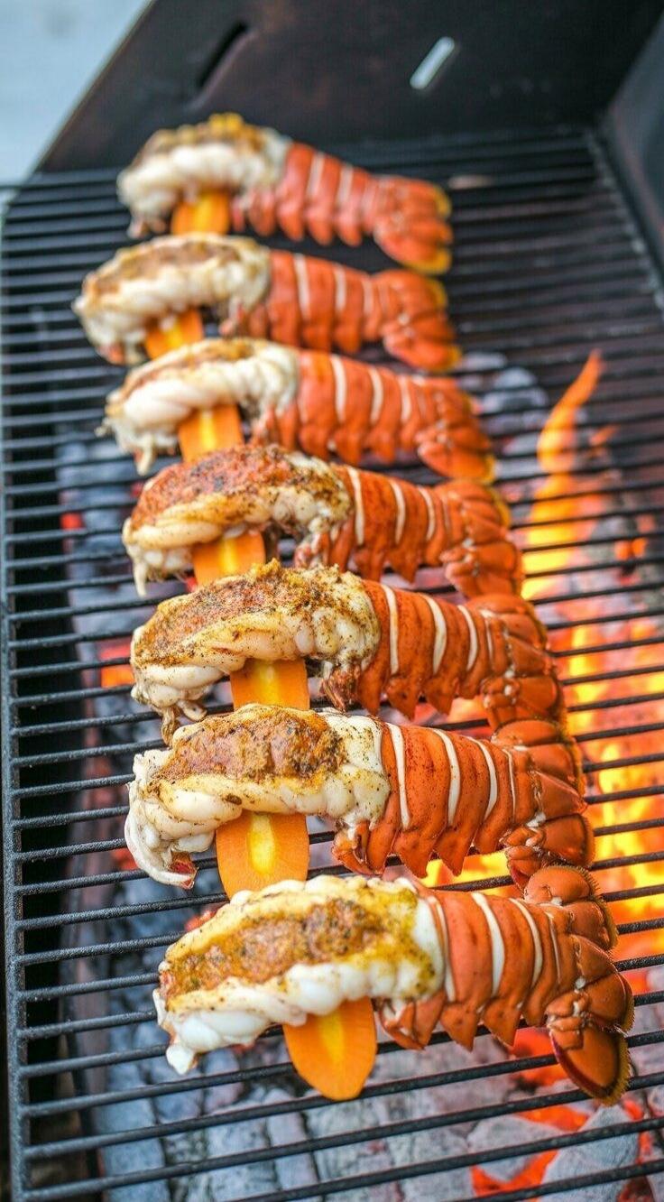 Grilled lobster tails skewered with orange peppers cooking on a barbecue grill.