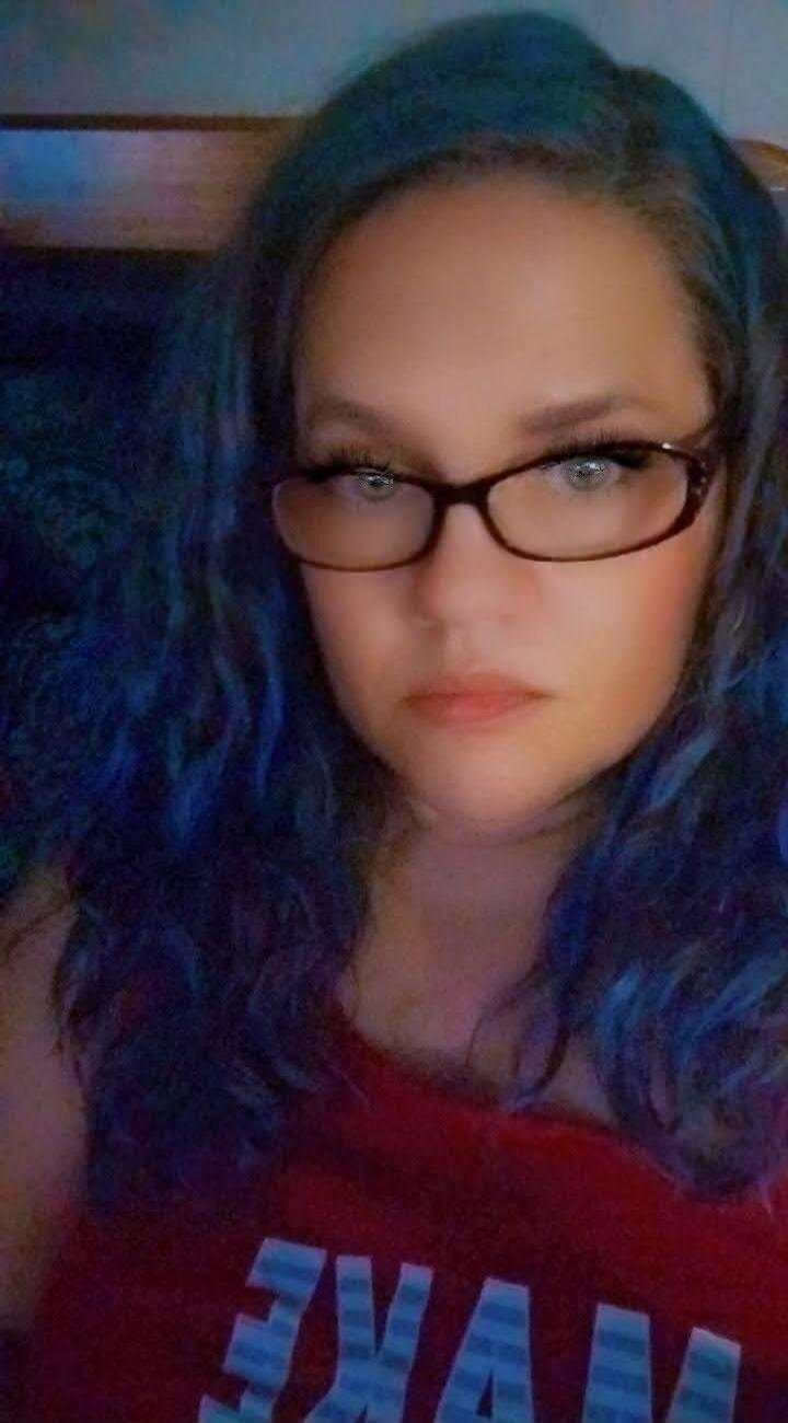 A woman with blue hair and glasses wearing a red top with 'NIKE' text.