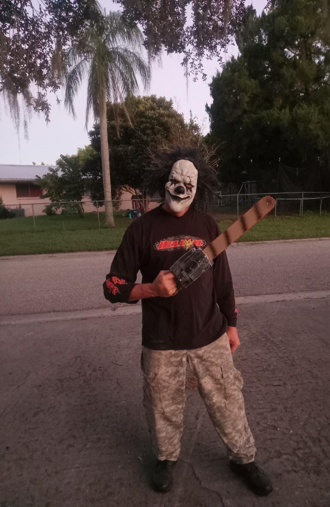 Person wearing a creepy mask holding a chainsaw prop on a street.