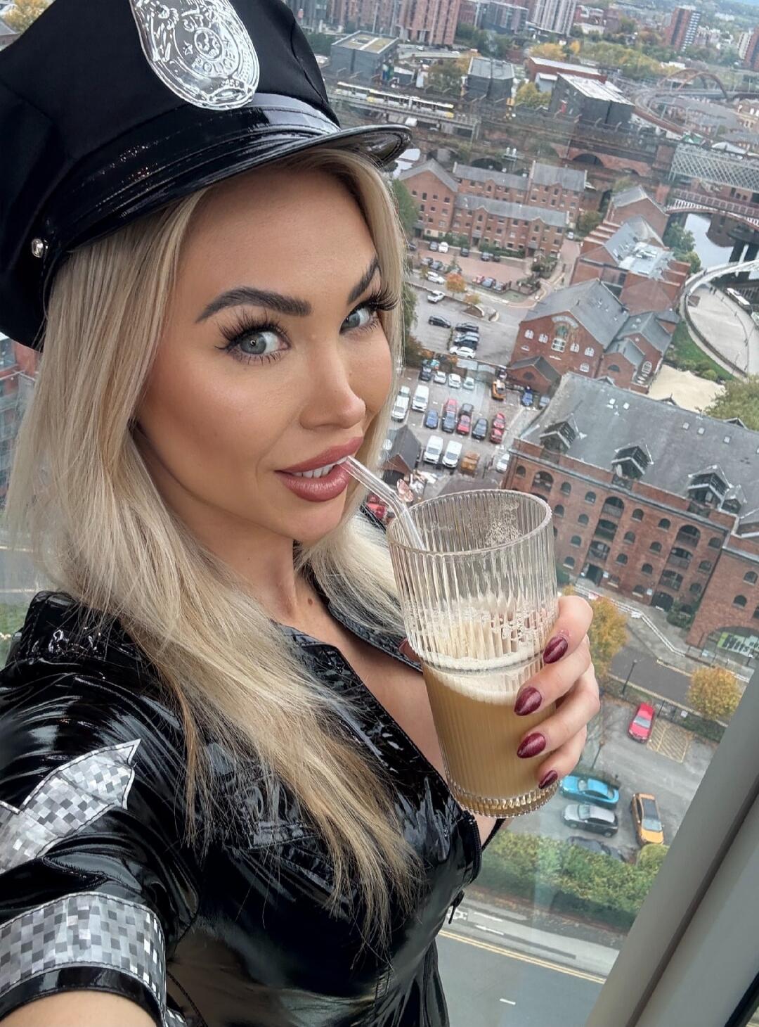 A woman in a police hat sipping a beverage through a straw while overlooking a city from a high-rise.