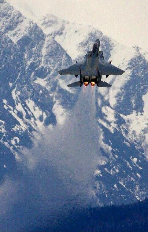 Fighter jet with afterburners taking off over snowy mountains.