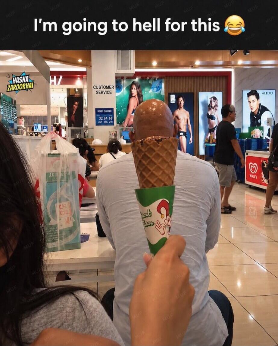 I'm going to hell for this 😂. A person is holding an ice cream cone behind a bald man's head, making it appear as if the ice cream is on his head. In the background, there are various advertisements, including some featuring models in swimwear.
