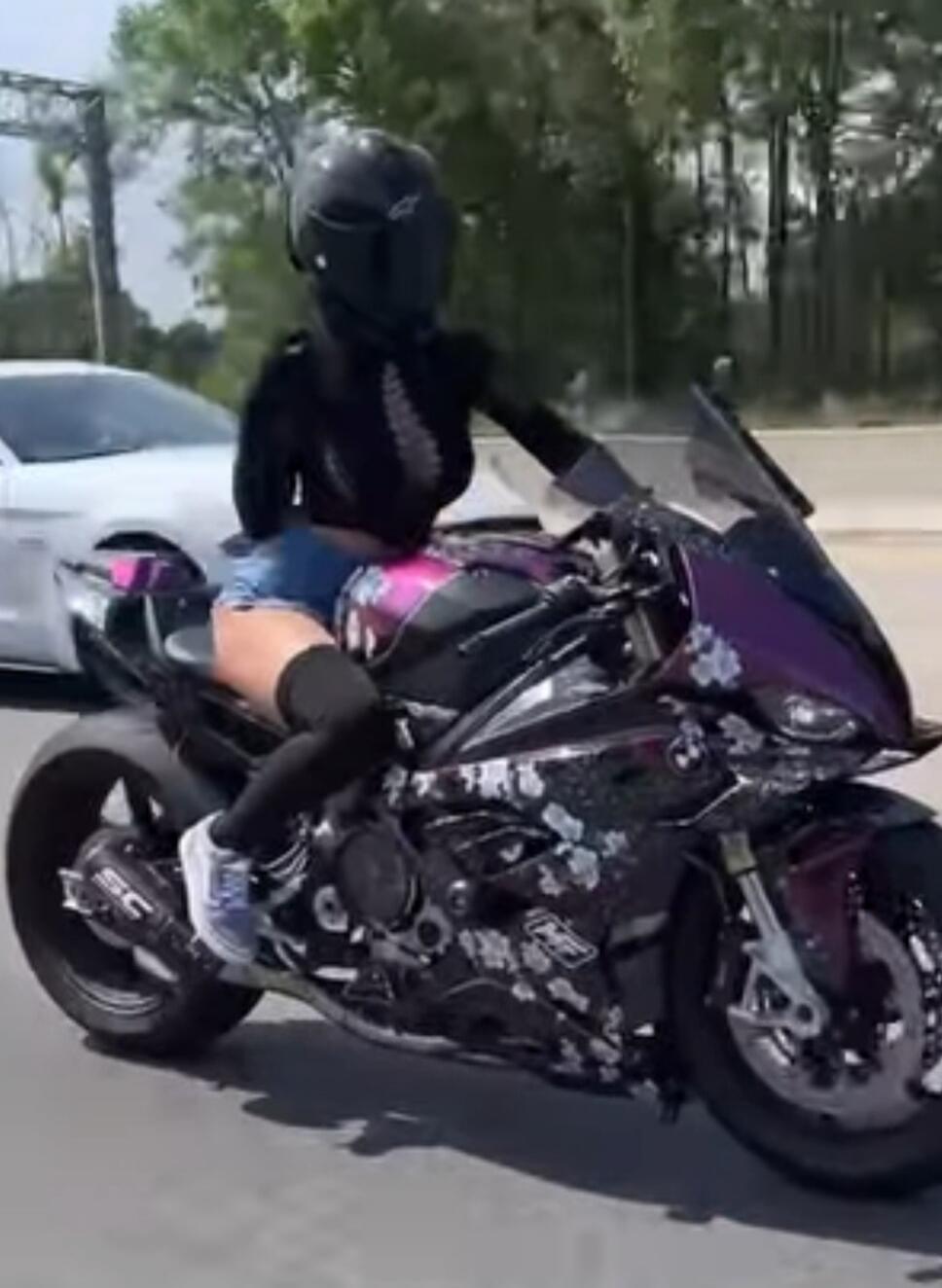 A motorcyclist wearing a full-face helmet riding a purple sport motorcycle on a road.