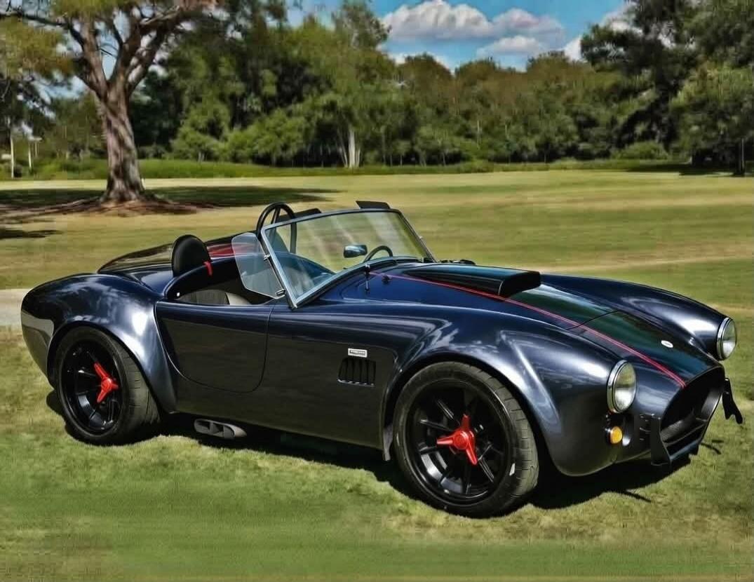 A classic dark blue Shelby Cobra car parked on a grassy field with trees in the background.