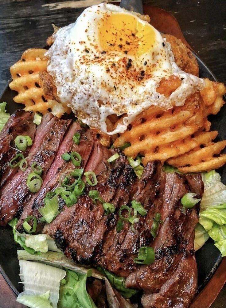 A delicious meal of sliced steak, waffle fries, and a fried egg on top.