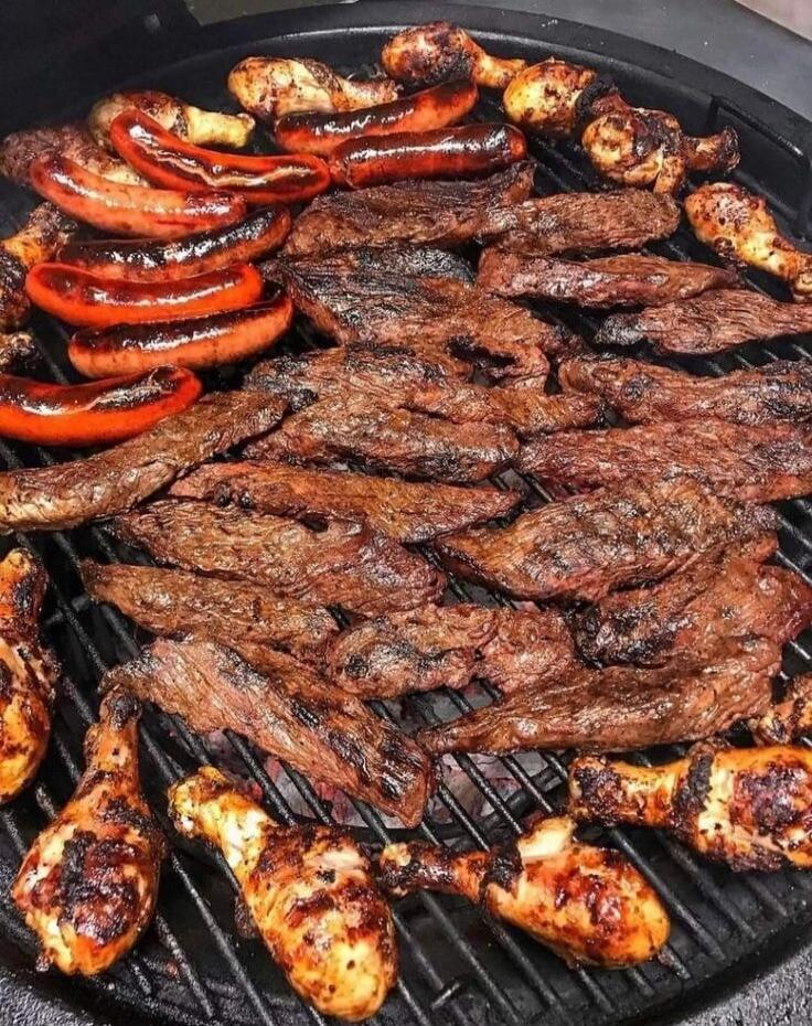 Assorted grilled meats on a barbecue grill: strips of beef, chicken pieces, and red bell peppers.