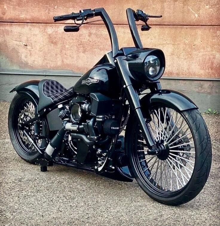 Custom black cruiser motorcycle with large front wheel, upward-swept handlebars, matte finish, and intricate spoke wheels.