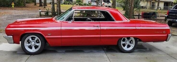 Red classic car (lowrider) with white rims parked on a driveway.
