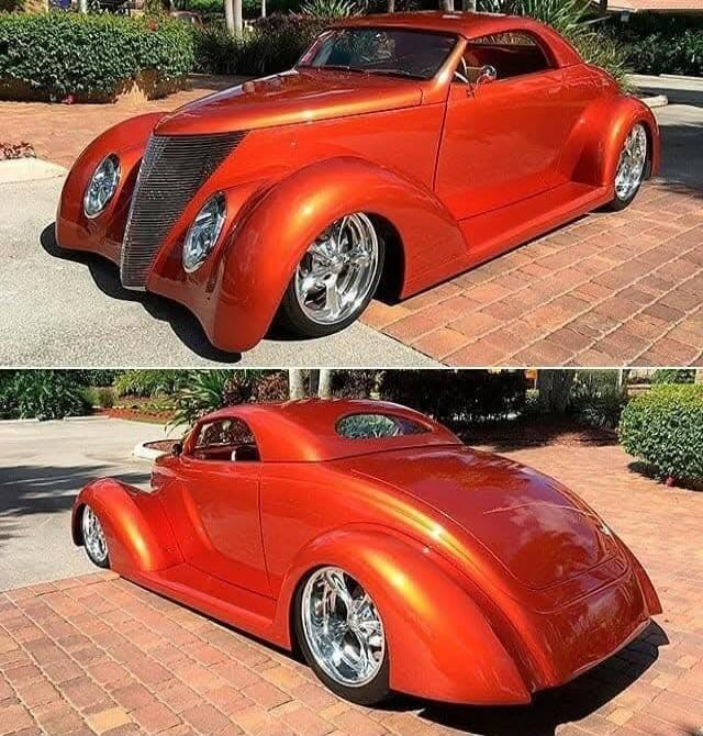 Orange custom classic car with rounded, streamlined body and chrome wheels.