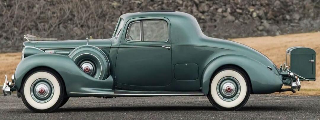 A vintage green coupe car with white wall tires and a spare tire mounted on the side.