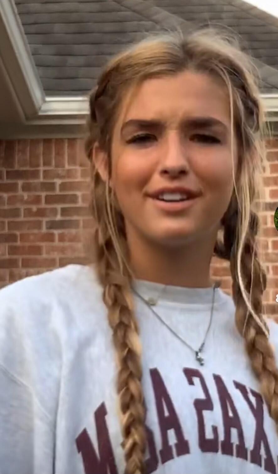 A young woman with blonde braided hair, wearing a light-colored sweatshirt with the word 'TEXAS' printed in reverse.