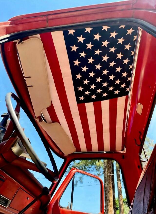 Red vehicle interior with an American flag stretched across the roof inside the open-door cabin.