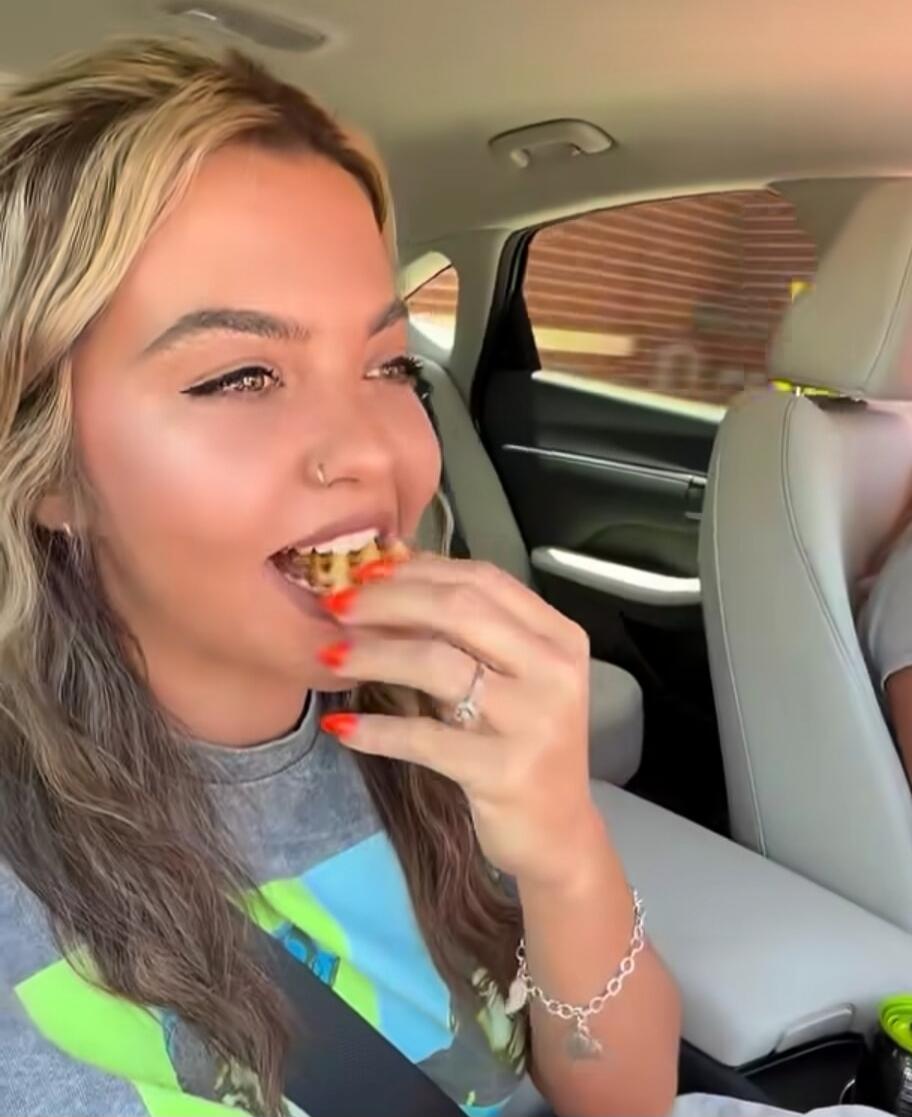 A woman in a car eating a snack.