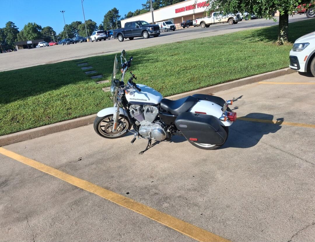A white Harley-Davidson motorcycle is parked in a lot. In the background, a building with 'HARBOR FREIGHT TOOLS' signage is visible.