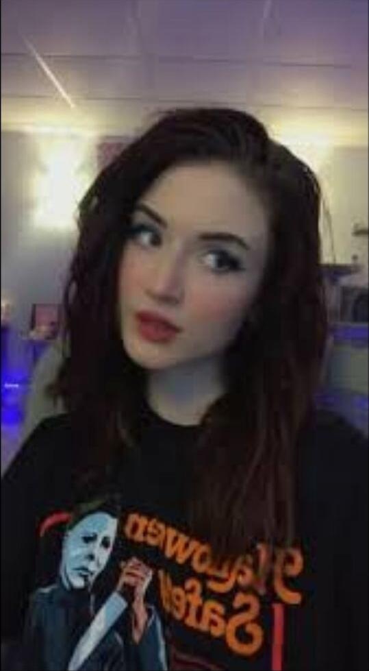 A young woman with dark hair wearing a black t-shirt with an orange graphic image of a man.